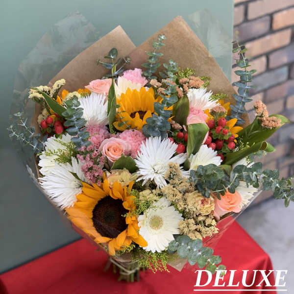 Mixed bouquet with sunflowers, white daisies, and pink roses wrapped in brown paper