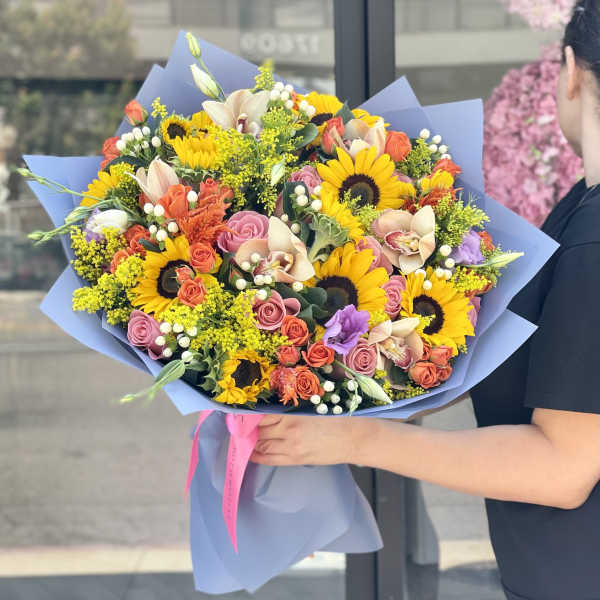 Large bouquet of sunflowers, roses, and orchids wrapped in blue paper
