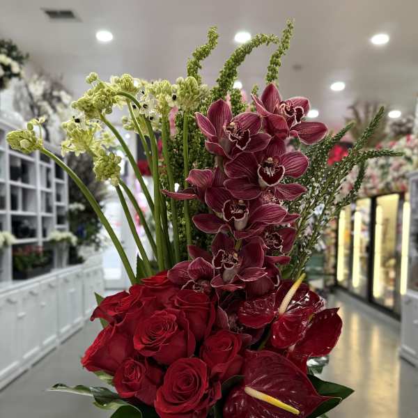 Red roses and burgundy orchids in a tall glass vase