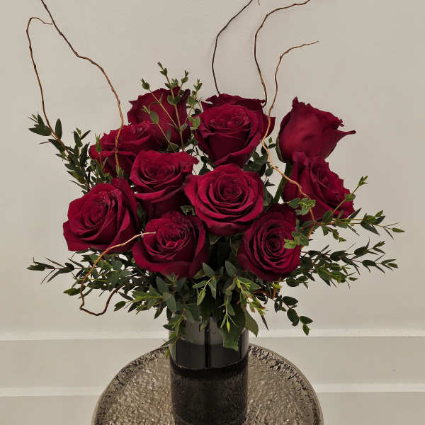 Deep red roses arranged in a black vase with curly branches