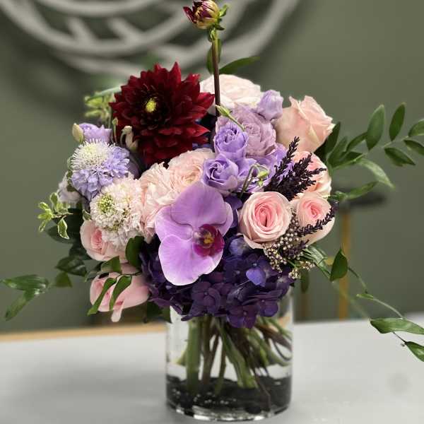 Mixed pink, purple, and burgundy flowers arranged in a clear glass vase