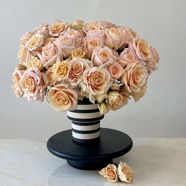 Peach and blush roses arranged in a striped vase on a black stand