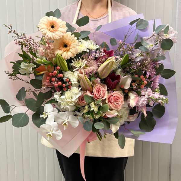 Large pastel bouquet with roses, lilies, and gerbera daisies wrapped in pink and lavender paper