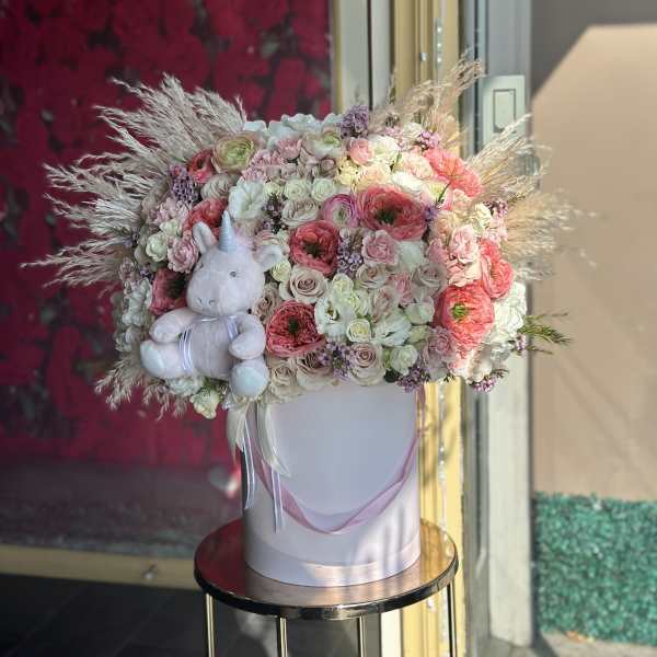 Pastel flower arrangement in a white hatbox with a plush unicorn