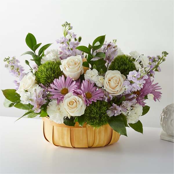 Mixed bouquet of white roses and purple daisies in a woven basket
