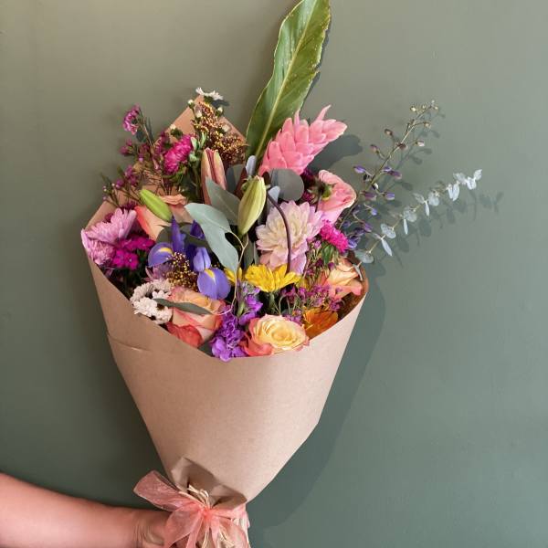 Colorful mixed flower bouquet wrapped in brown paper with a pink ribbon