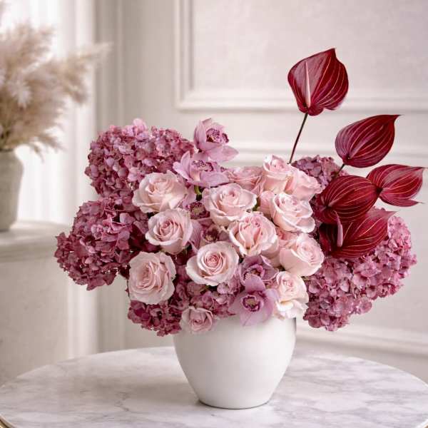 Pink rose, hydrangea, and orchid arrangement with burgundy accents in a white vase on a marble table