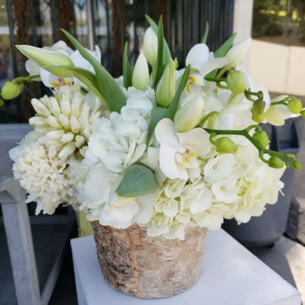 White floral arrangement in a birch bark container with orchids and lilies