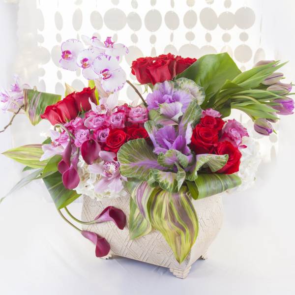Mixed bouquet of red roses, pink orchids, and calla lilies in a white vase