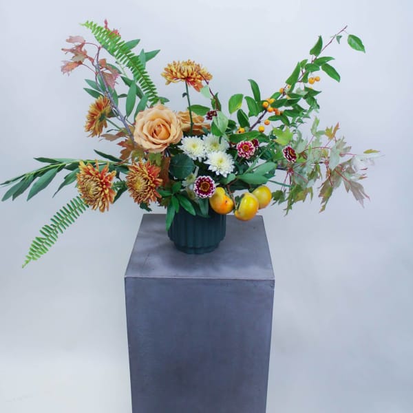 Mixed floral arrangement in a dark vase with peach roses and orange chrysanthemums