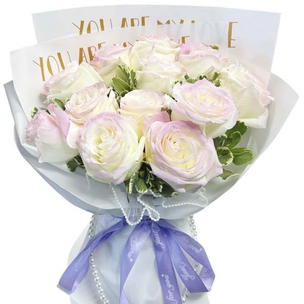 Bouquet of pale pink and white roses wrapped in white paper with a purple ribbon
