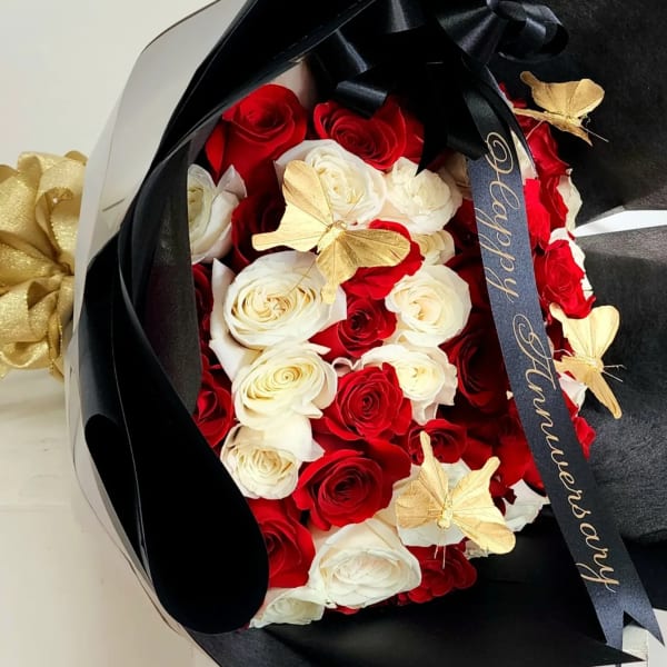 Bouquet of red and white roses wrapped in black paper with gold butterfly accents