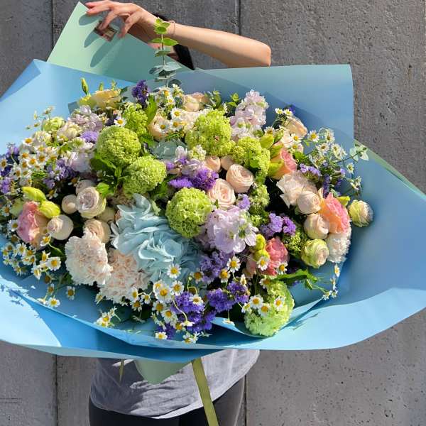 Large pastel bouquet with roses, carnations, and daisies wrapped in blue paper