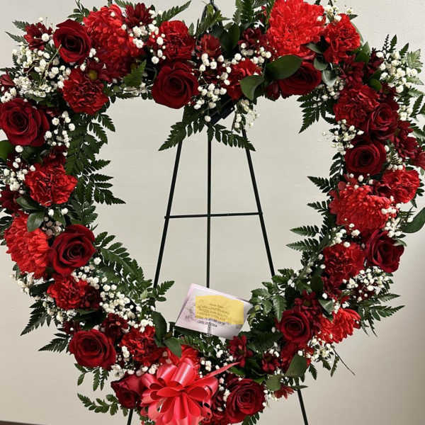 Heart-shaped red floral wreath on an easel with a pink bow