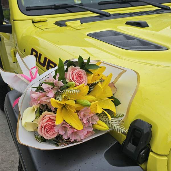 Bouquet of pink roses, yellow lilies, and pale pink flowers wrapped in white paper