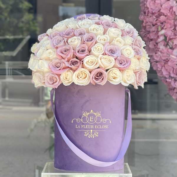 Round bouquet of pink and white roses in a purple hatbox