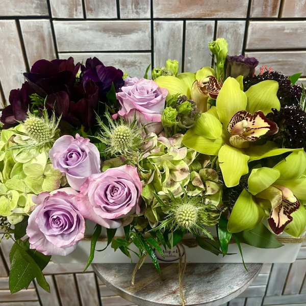 Mixed bouquet with lavender roses and bright green orchids in a white container