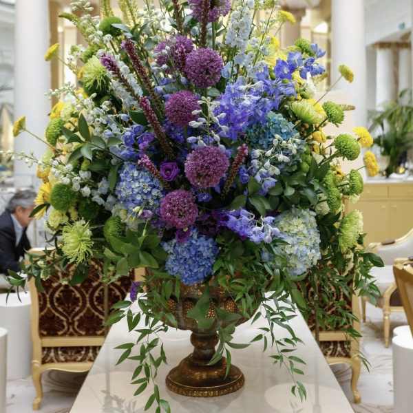 Large mixed floral centerpiece in a pedestal vase with purple, blue, yellow, and green blooms