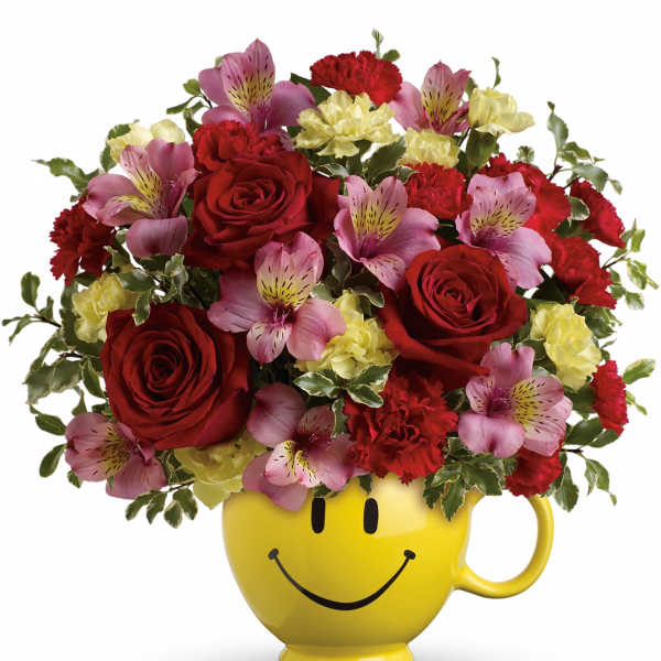 Bouquet of red roses, pink alstroemeria, and yellow carnations in a smiley-face mug