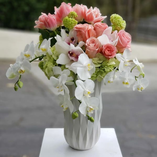 Pink roses and white orchids arranged in a white vase