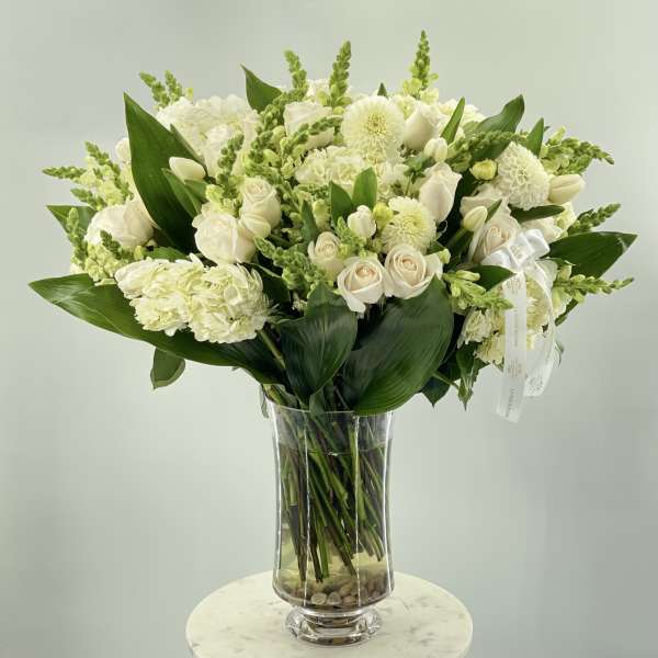 White floral arrangement in a clear glass vase with broad green leaves