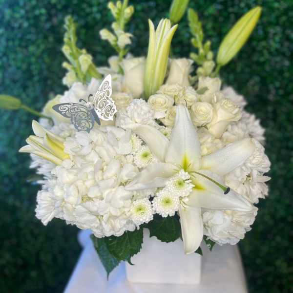 White floral arrangement with lilies and roses in a square vase
