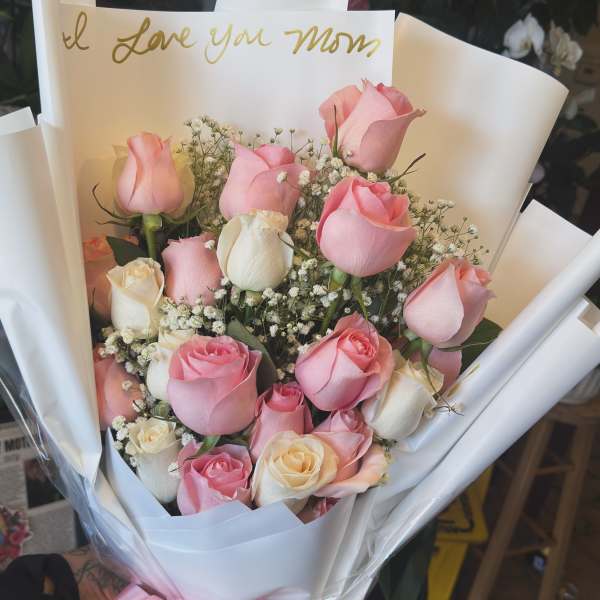 Bouquet of pink and white roses wrapped in white paper with a pink bow