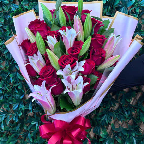 Bouquet of red roses and pink lilies wrapped in white paper with a red bow