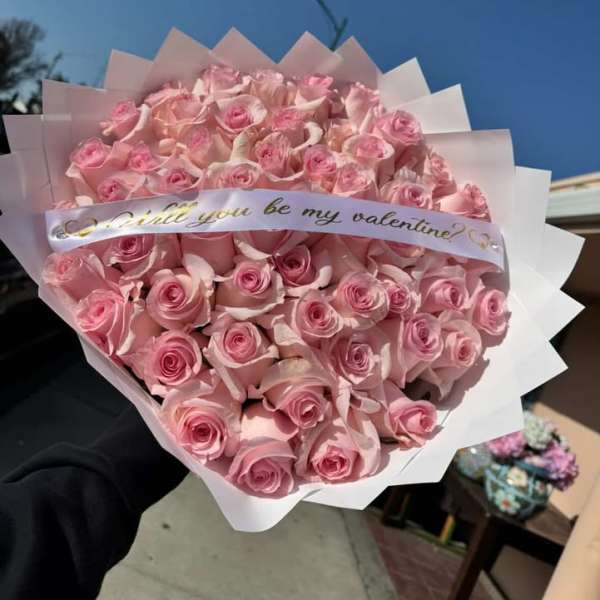 Large bouquet of pink roses wrapped in white paper with a Valentine ribbon