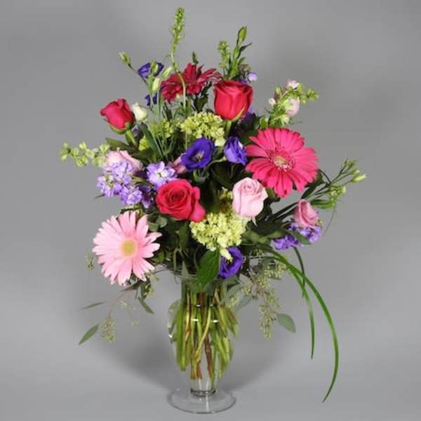 Mixed bouquet of pink, purple, and red flowers in a clear glass vase
