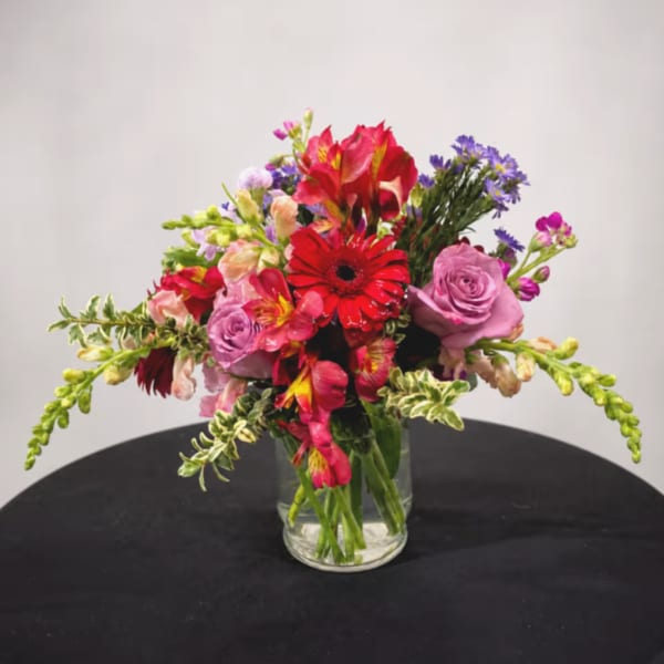 Mixed bouquet of red, pink, and purple flowers in a clear glass vase