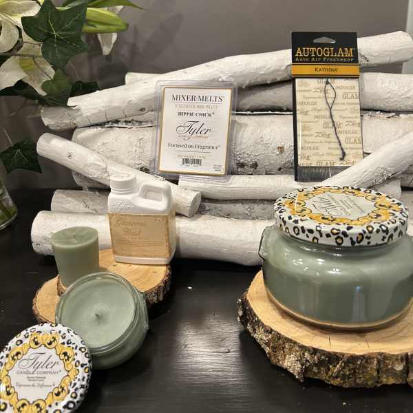 Assorted candles and fragrance products arranged on wood slices with white branches.