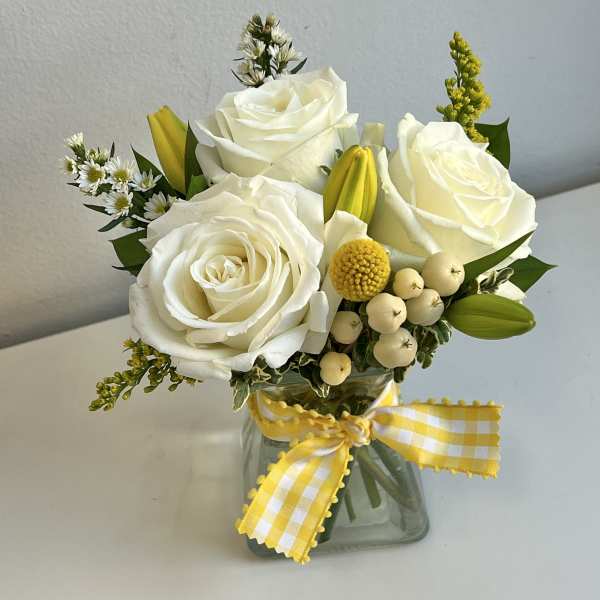White roses and yellow accents in a glass vase with a gingham ribbon