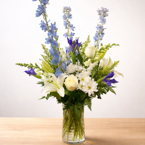 Tall mixed bouquet in a glass vase with blue, white, and purple flowers
