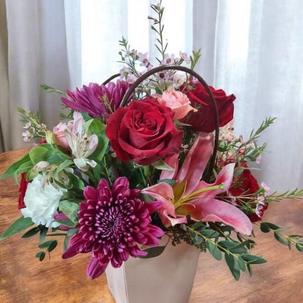Mixed flower arrangement in a white handled box with red roses and pink lilies