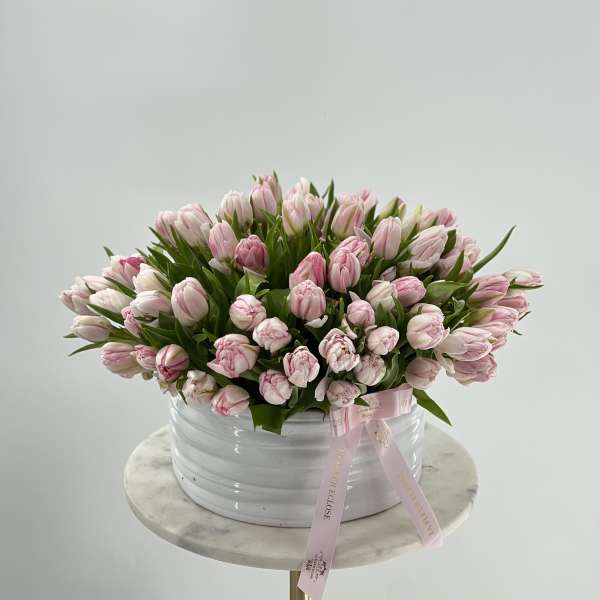 Pink tulips arranged in a white round container with a pink ribbon