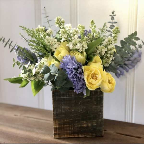 Yellow and lavender flowers arranged in a square wooden vase