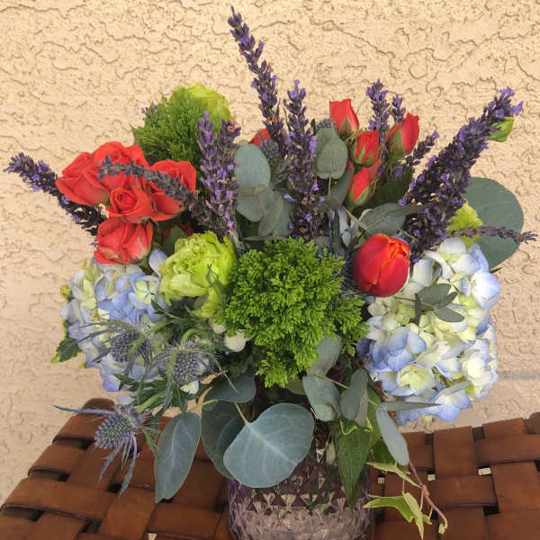 Bouquet of red roses, blue hydrangeas, and purple lavender in a glass vase