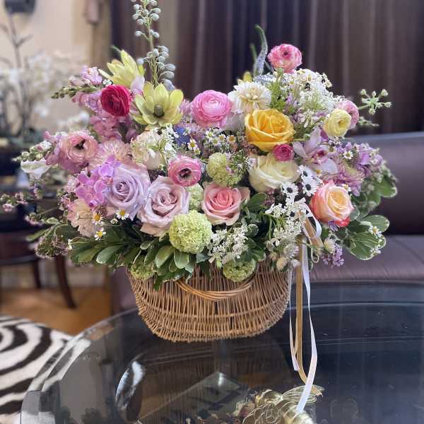 Mixed pastel flower arrangement in a wicker basket with ribbon ties