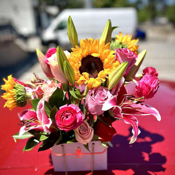 Bright bouquet of pink roses, lilies, and sunflowers in a white box