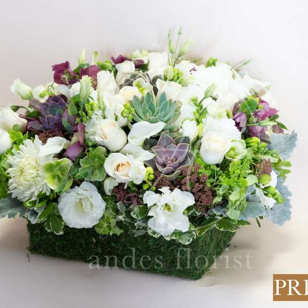 White and purple floral arrangement in a rectangular moss-covered container