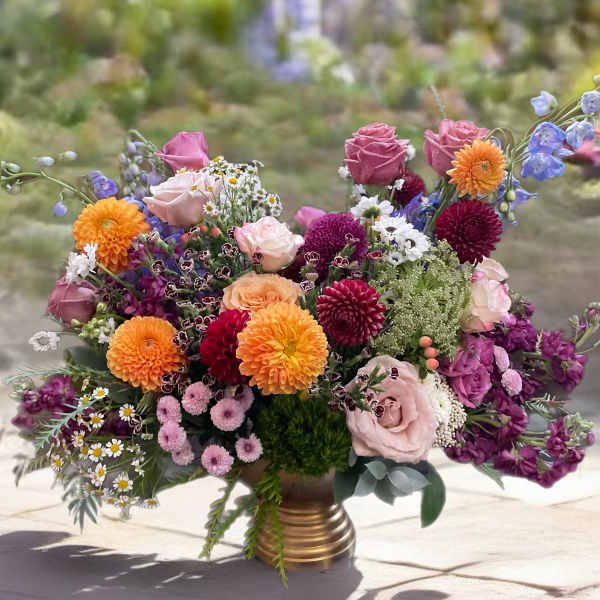 Colorful mixed bouquet in a gold vase with pink, orange, and purple blooms
