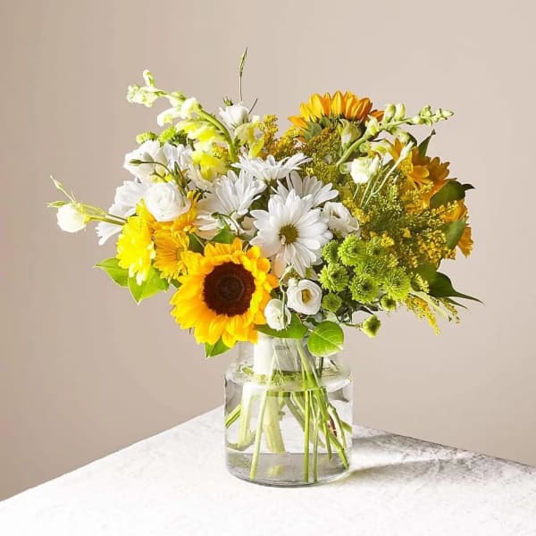 Bouquet of sunflowers, white daisies, and yellow flowers in a glass vase