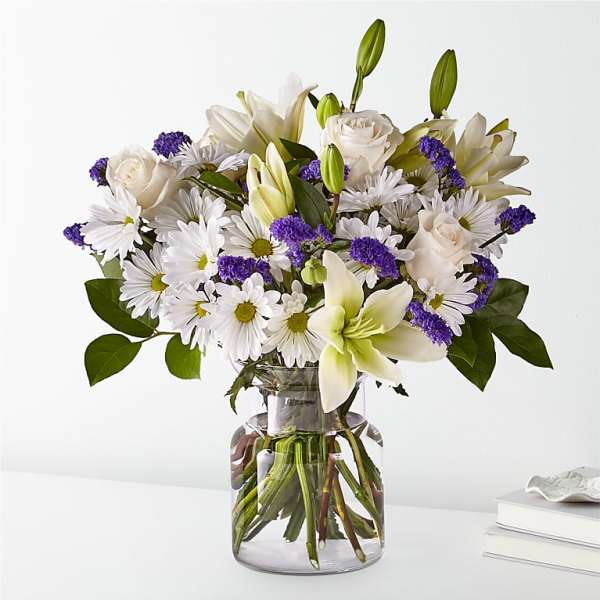 White lilies, roses, and daisies in a clear glass vase