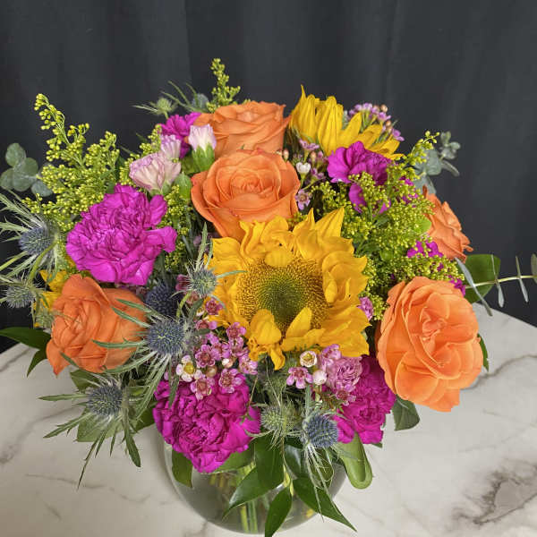Bouquet of orange roses, yellow sunflower, and bright pink flowers in a glass vase