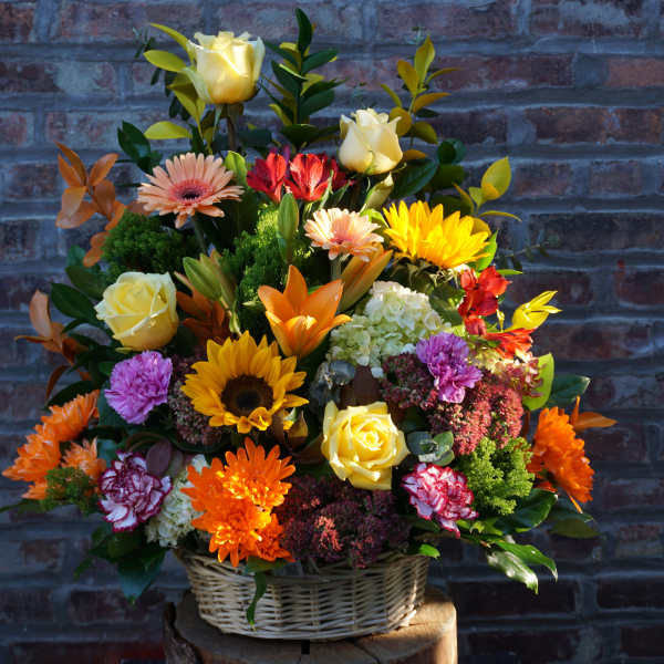 Mixed flower arrangement in a wicker basket with yellow roses and bright daisies