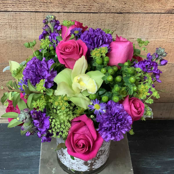 Pink roses and purple flowers arranged in a rustic white vase