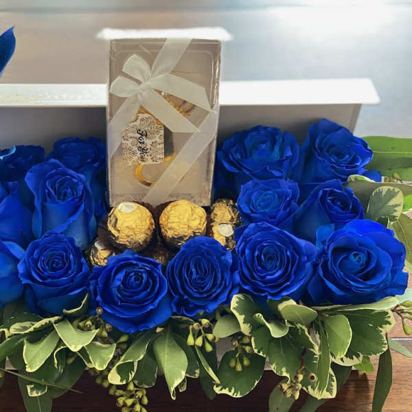 Blue roses arranged around a gift box and chocolates