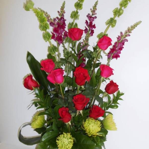 Tall bouquet of red and pink roses with green and purple spikes in a black vase