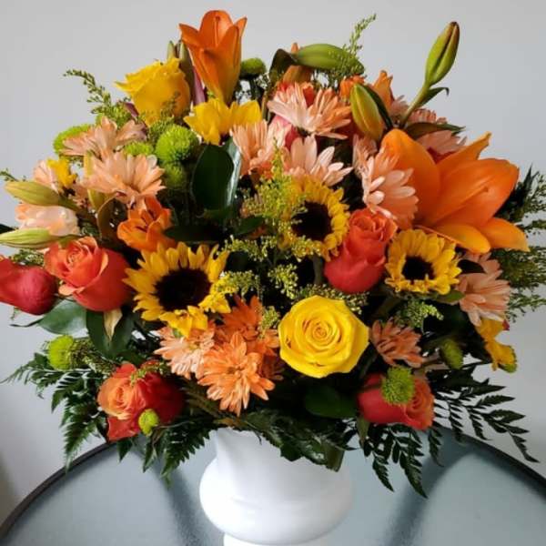 Mixed bouquet of orange, yellow, and pink flowers in a white vase